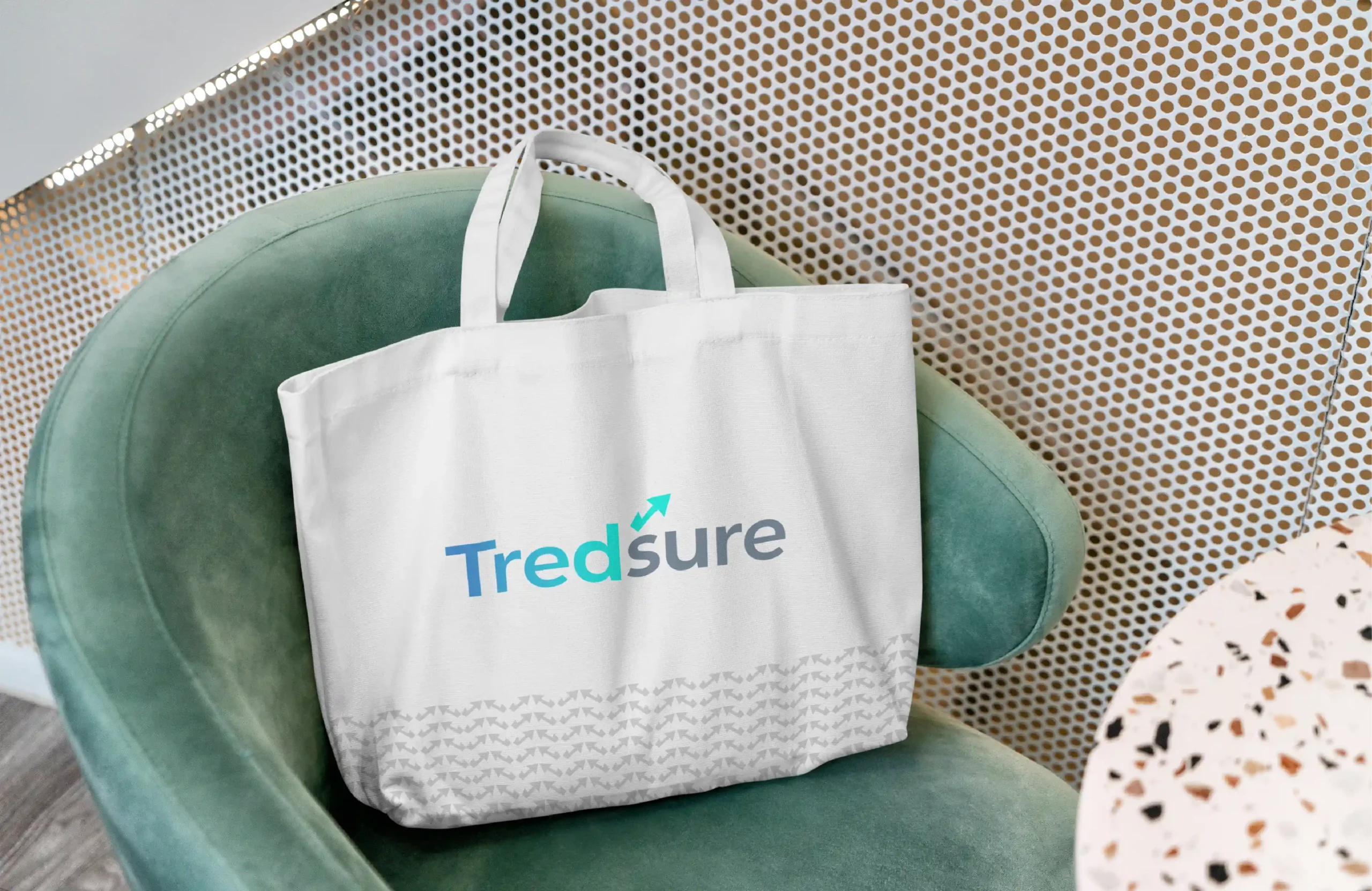 White tote bag with Tredsure logo placed on a green chair, showing finance brand merchandise design.