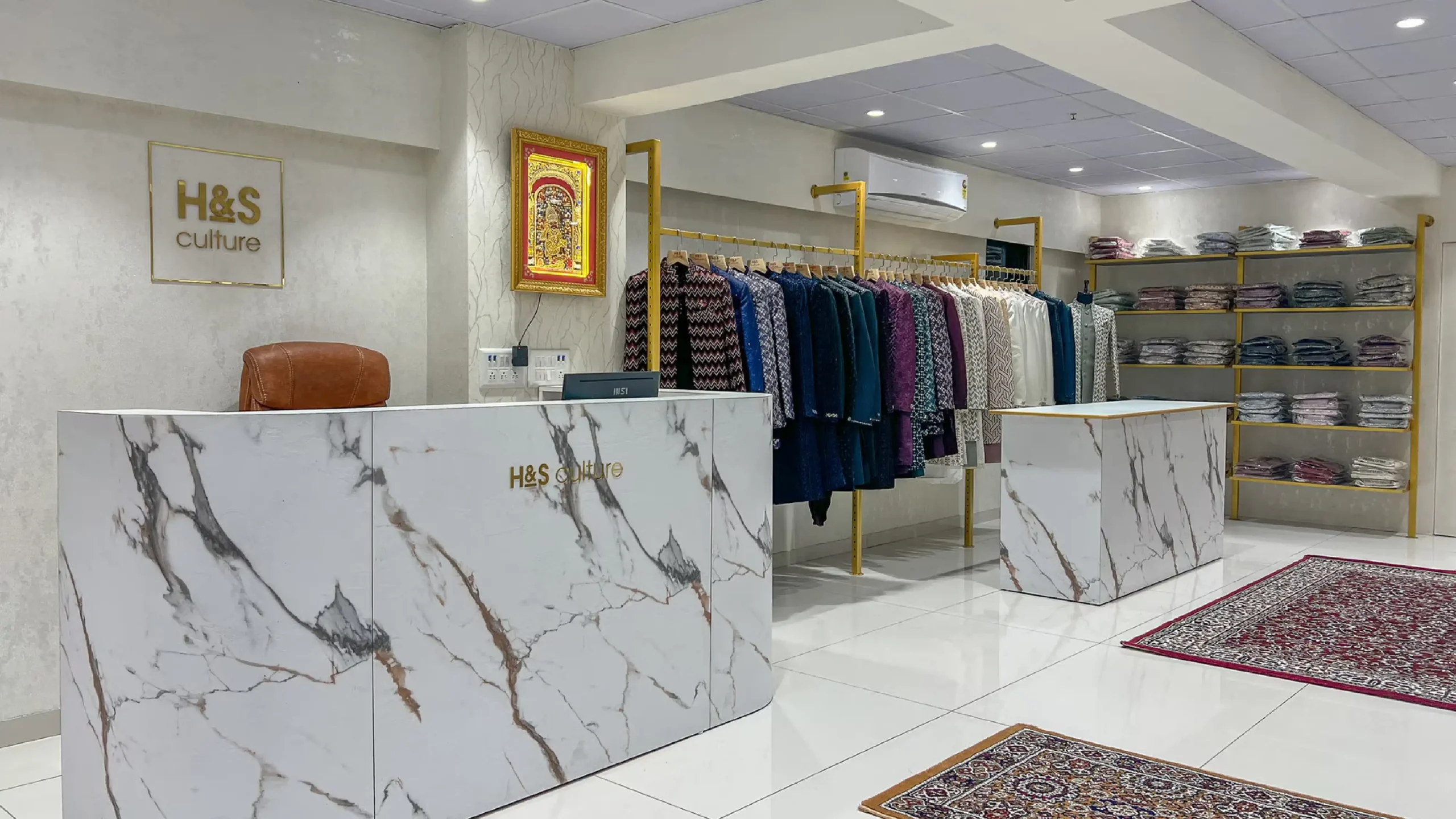 Reception area of H&S Culture ethnic fashion showroom with marble counter, branded wall, designer menswear display, and luxury interior
