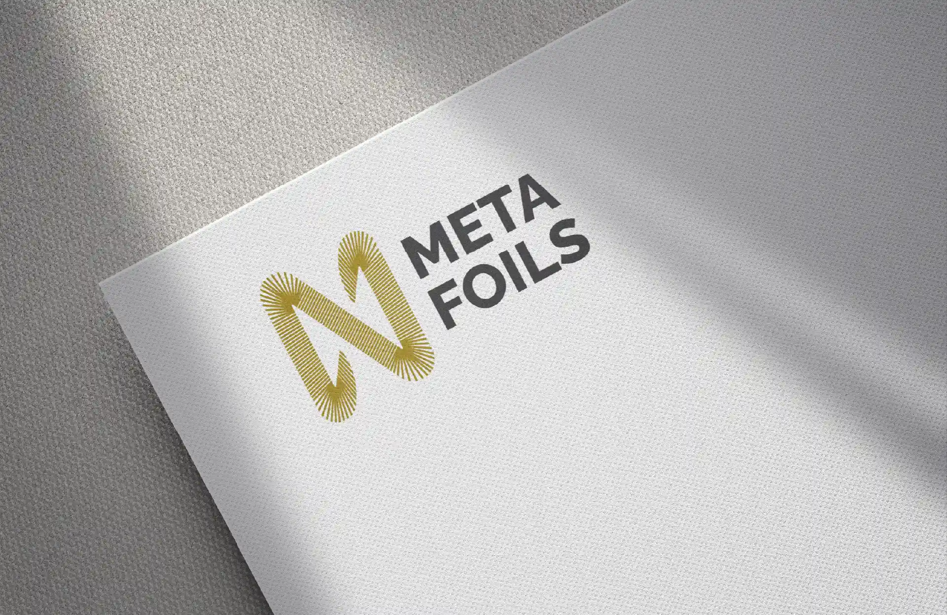 http://Meta%20Foils%20logo%20design%20printed%20on%20textured%20white%20paper%20with%20a%20gold%20abstract%20monogram%20and%20bold%20brand%20typography.