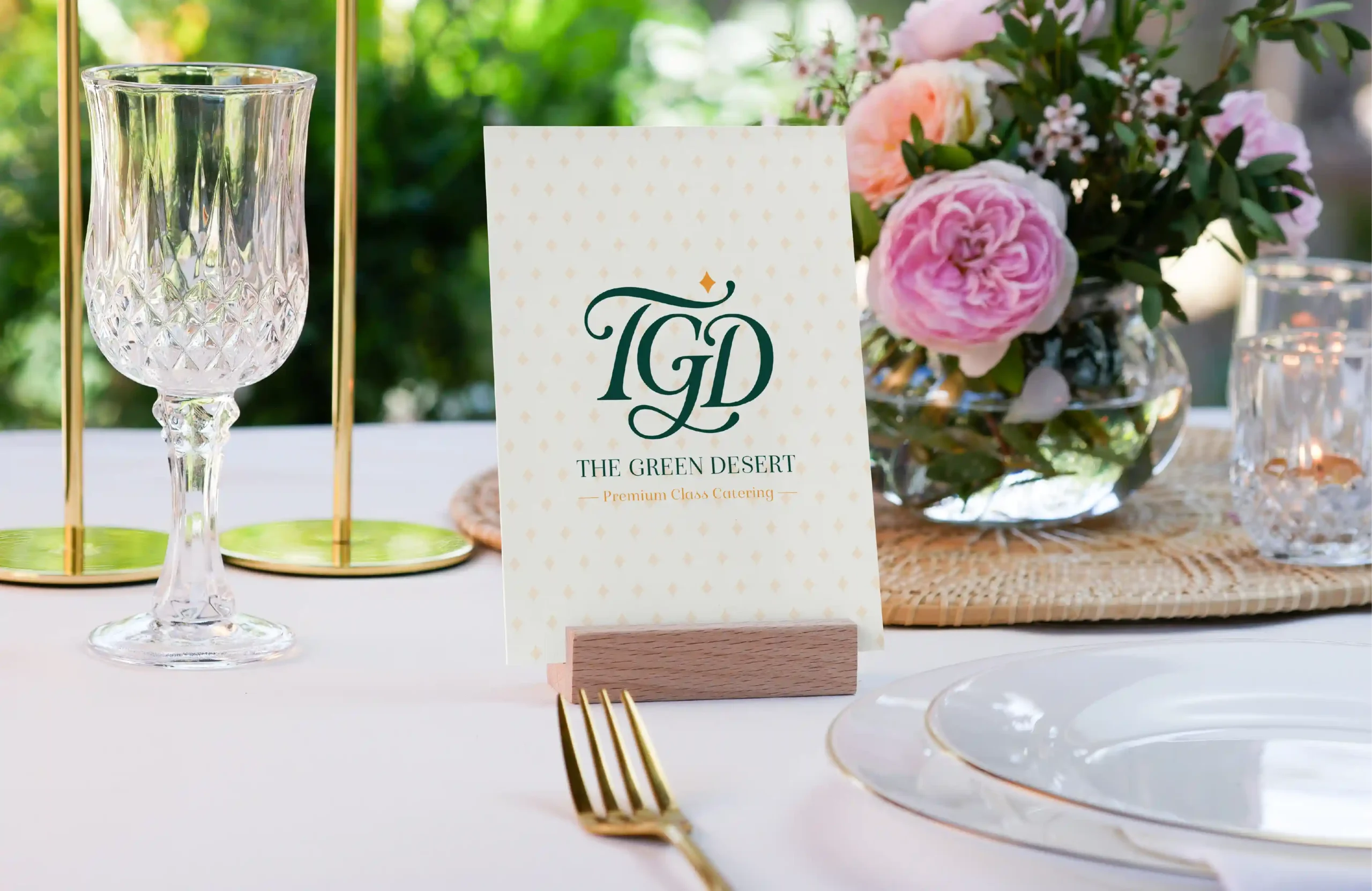 The Green Desert catering menu card displayed on an elegant table with glassware and pink floral arrangements.